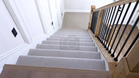 Téléchargez les photos : L'image capture le détail d'un escalier moderne bien conçu, doublé d'un tapis beige moelleux, complété par des murs blancs et des balustres en bois. - en image libre de droit