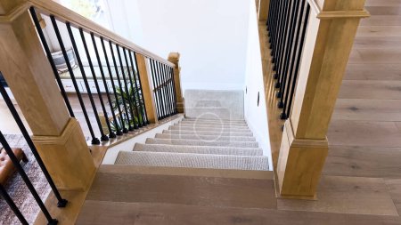 Foto de La imagen captura el detalle de una escalera moderna bien diseñada, forrada con una lujosa alfombra beige, complementada con paredes blancas y balaustres de madera.. - Imagen libre de derechos