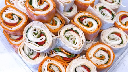 Téléchargez les photos : Un étalage alléchant de sandwichs aux pinwheel remplis de légumes frais et de charcuteries, parfait pour tout rassemblement ou déjeuner rapide. - en image libre de droit