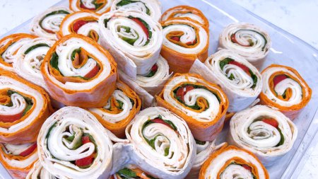 A mouthwatering display of pinwheel sandwiches filled with fresh greens and deli meats, perfect for any gathering or quick lunch.