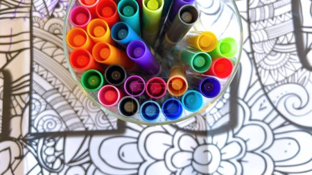Photo for A kaleidoscopic collection of markers in a clear holder, poised above a detailed line drawing, invites a burst of artistic inspiration. - Royalty Free Image