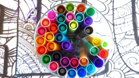 A kaleidoscopic collection of markers in a clear holder, poised above a detailed line drawing, invites a burst of artistic inspiration.