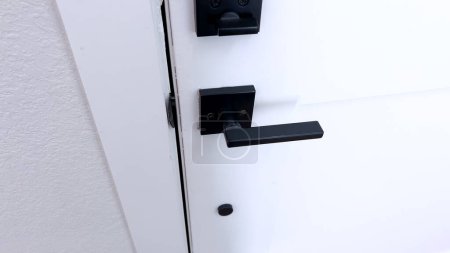 A close-up of a sleek black door handle mounted on a crisp white door, highlighting a minimalist and contemporary home design.