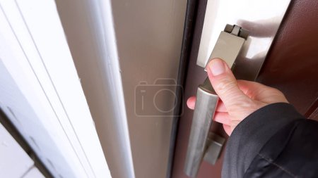 Foto de Una mano de persona es capturada en el proceso de abrir una puerta usando un mango de metal cepillado, retratando la acción de entrar o salir de una habitación. - Imagen libre de derechos