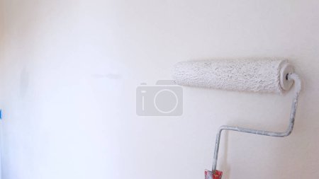 Téléchargez les photos : Mur partiellement peint avec un rouleau de peinture blanc, mettant en valeur le processus de rénovation murale et d'amélioration de la maison. - en image libre de droit