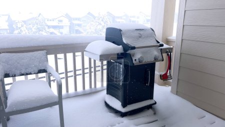 Foto de Capas gruesas de nieve cubren un balcón con muebles de exterior, ofreciendo una vista serena de un paisaje suburbano envuelto en abrazos de invierno. - Imagen libre de derechos