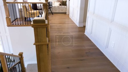 Téléchargez les photos : À l'intérieur d'une élégante maison, des planchers de bois franc poli guident le chemin à travers un couloir orné de lambris sophistiqués. Les tons chauds de bois de la rampe complètent l'invitant et haut de gamme - en image libre de droit