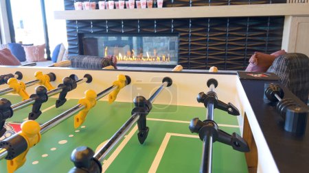 Photo for Foosball table, poised for a friendly match, with figures lined up and ready for play, set against a backdrop of a glowing fireplace, creating a cozy leisure setting. The scene invites warmth and - Royalty Free Image
