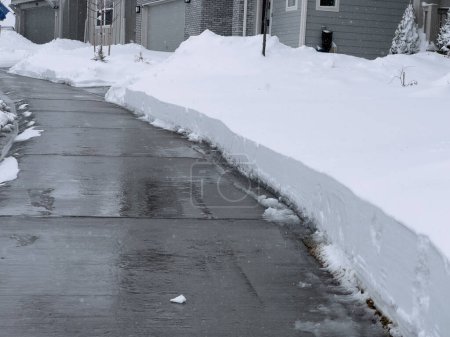 A solitary pathway cuts through a blanket of snow in a quiet residential neighborhood, leading to a welcoming home. The overcast sky and untouched snowdrifts capture the stillness of a winter day.