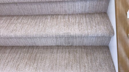This image captures a detail of a home interior, focusing on the texture and pattern of beige carpeted stairs meeting a polished hardwood landing.