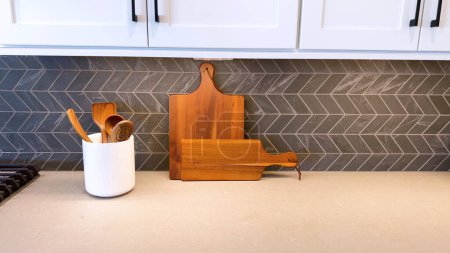 A contemporary kitchen setup showcasing a pristine countertop, stylish herringbone tile backsplash, and essential cooking utensils in a chic white holder alongside a wooden cutting board, combining