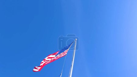 Téléchargez les photos : Une image saisissante du drapeau américain flottant dans le vent, placé contre un ciel bleu vif avec amplement d'espace de copie, symbolisant le patriotisme et la fierté nationale. - en image libre de droit