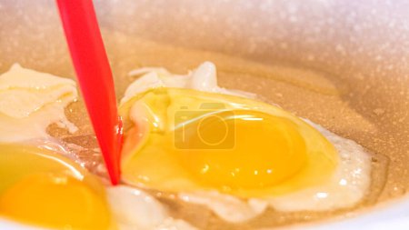 Photo for Vibrant yolks shine, red spatula amidst cooking eggs in speckled pan. - Royalty Free Image