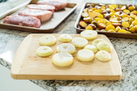 On a wooden cutting board, a fresh yellow onion is being neatly sliced. These uniform pieces are destined for the grill, where they will transform under the flame, offering a caramelized sweetness to