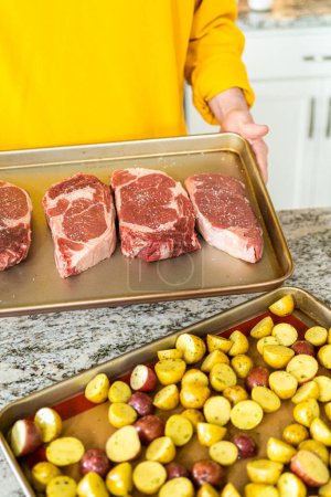 Photo for Situated in a modern white kitchen, a seasoned rib eye steak, boasting its beautiful marbling, sits ready on a baking sheet. It is prepared for the outdoor gas grill, promising a perfect sear on the - Royalty Free Image