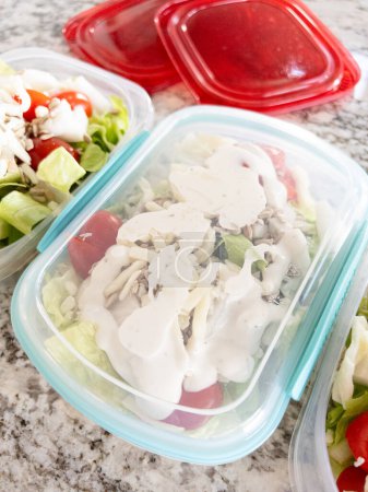 Behälter gefüllt mit Salat und Dressing, zubereitet für eine bequeme Mittagsmahlzeit.