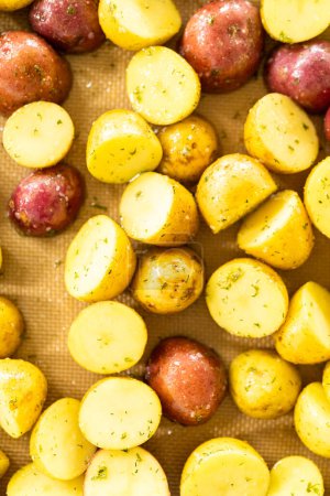 In a modern kitchen, an array of halved, multicolored marble potatoes are arranged on a baking pan lined with a silicone liner. The roasting process infuses the kitchen with a mouthwatering aroma