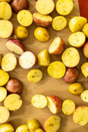 In a modern kitchen, an array of halved, multicolored marble potatoes are arranged on a baking pan lined with a silicone liner. The roasting process infuses the kitchen with a mouthwatering aroma