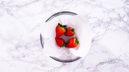 Téléchargez les photos : Pose plate. Les fraises fraîchement lavées et séchées sont soigneusement disposées dans un bol en verre doublé d'une serviette en papier, prêtes à être grignotées ou utilisées ultérieurement.. - en image libre de droit