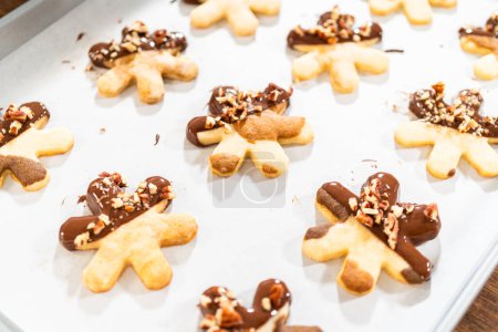 Foto de Creación de galletas de azúcar cortadas en forma de copo de nieve, sumergidas en chocolate, y adornadas con nueces de pacana trituradas, elegantemente presentadas en pergamino. - Imagen libre de derechos