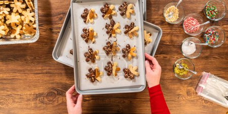 Photo for Creating snowflake-shaped cutout sugar cookies, dipped in chocolate, and adorned with crushed pecan nuts, elegantly presented on parchment. - Royalty Free Image