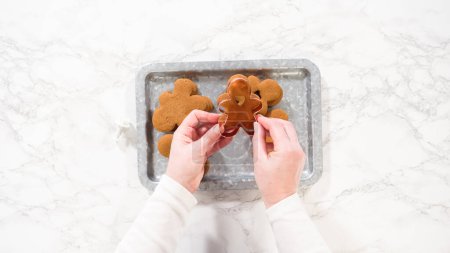 Flat lay. Gingerbread cookies, including a gingerbread man with a heart-shaped cutout, rest on a rustic metal tray against a marble countertop.
