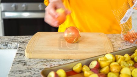 In the welcoming setting of a modern kitchen, a young man continues his dinner preparation process. Hes currently involved in slicing yellow onions into rings, prepping them for grilling on an
