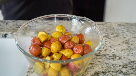 In a sleek, modern kitchen, a young man attentively prepares dinner. His current task involves carefully seasoning small rainbow potatoes in a glass bowl, promising a flavorful meal ahead.