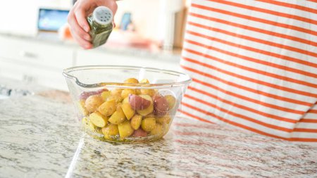 In a sleek, modern kitchen, a young man attentively prepares dinner. His current task involves carefully seasoning small rainbow potatoes in a glass bowl, promising a flavorful meal ahead.