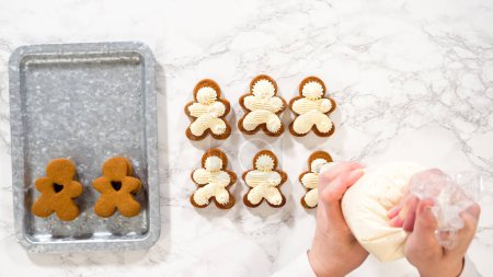 Flat lay. Gingerbread cookies await their second halves on a marble surface, each meticulously piped with buttercream to craft delightful sandwich treats. The precision of the piping adds a festive