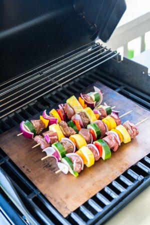 Téléchargez les photos : Broche de bœuf et légumes frais grésille sur un tapis de gril en cuivre sur un barbecue extérieur au gaz. - en image libre de droit