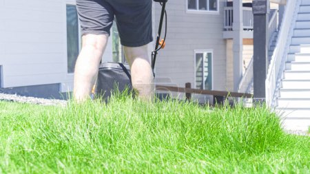 Téléchargez les photos : Dans une maison de banlieue résidentielle, une pelouse verte luxuriante est soigneusement tondue à l'aide d'une tondeuse à gazon électrique, créant un espace extérieur bien entretenu et accueillant. - en image libre de droit
