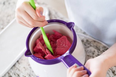 Photo for Eager eyes focus on the pot of vibrant, melting candy as a young cook gently swirls the mixture, poised to transform plain snacks into delectable treats. - Royalty Free Image