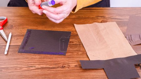 Schritt für Schritt. Der Lehrer führt den Online-Unterricht durch die Herstellung einer Papierpuppe aus einer braunen Tasche, wobei er eine Holzoberfläche kreativ als Arbeitsplatz nutzt.