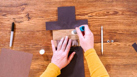 Step by step. Flat lay. Teacher guides online class through making a paper puppet from a brown bag, creatively using a wooden surface as a workspace.