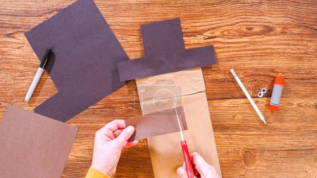 Schritt für Schritt. Flach lag er. Der Lehrer führt den Online-Unterricht durch die Herstellung einer Papierpuppe aus einer braunen Tasche, wobei er eine Holzoberfläche kreativ als Arbeitsplatz nutzt.