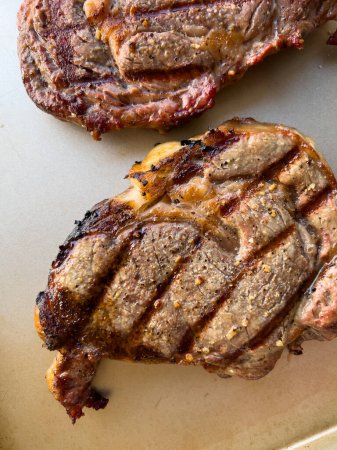 saftige Konsistenz von drei perfekt gegrillten Ribeye-Steaks mit verkohlten Rändern und ausgeprägten Grillspuren auf neutralem Hintergrund.