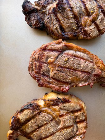 succulent texture of three ribeye steaks grilled to perfection, featuring charred edges and distinct grill marks, showcased on a neutral background.
