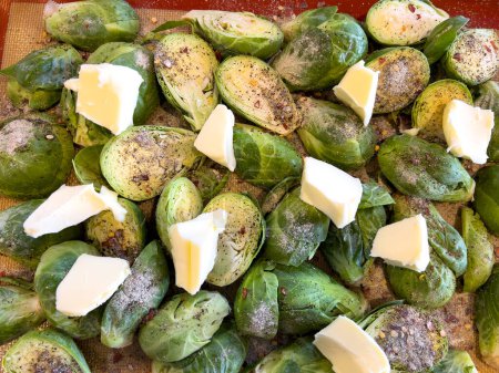 Photo for A tray of whole Brussels sprouts is generously topped with butter pats and seasoned, set against a non-stick baking sheet, indicating preparation for a savory roast. - Royalty Free Image