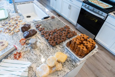 Téléchargez les photos : Les biscuits au pain d'épice fraîchement cuits trouvent leur place sur un support métallique de refroidissement dans une cuisine blanche moderne, remplissant l'air d'arômes festifs. - en image libre de droit