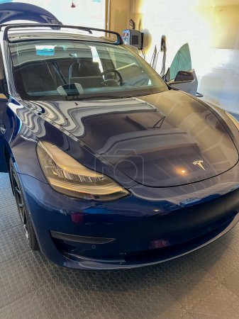 Photo for Castle Rock, Colorado, USA-March 14, 2024-A shiny blue Tesla Model 3 sits in the well-kept garage of a single-family house, its sleek design accentuated by the gentle care of a home car wash. - Royalty Free Image