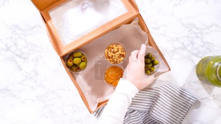 Photo for Flat lay. Hands are meticulously adding fresh red grapes to a bowl, complementing a beautifully arranged charcuterie box brimming with a variety of cheeses, olives, and cured meats, set against a - Royalty Free Image