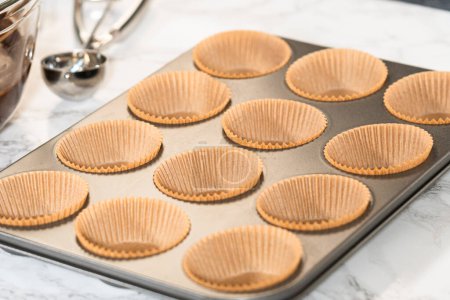 Getting ready to bake delicious chocolate cupcakes, we carefully line the cupcake pan with paper liners, ensuring a delightful treat awaits.