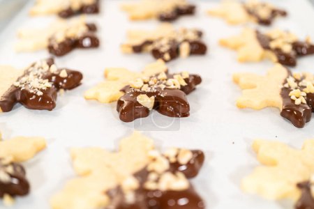 Foto de Creación de galletas de azúcar recortadas, parcialmente sumergidas en chocolate y cubiertas con trozos de avellana, colocadas en papel pergamino. - Imagen libre de derechos
