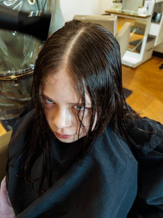 Las manos suaves maniobran un secador de pelo a través de un recién cortado pelo de las niñas, mostrando el proceso de secado después de un ajuste meticuloso. El calor de la secadora da vida a sus cerraduras, mientras se transforman