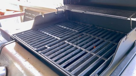 Sunlight illuminates an empty barbecue grill, its clean grates glistening and ready for a session of outdoor grilling, promising a delicious meal ahead.
