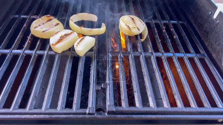 Steki Ribeye skwierczą obok złotej grillowanej cebuli na grillu, z odrobiną dymu na przyrządzanej uczcie. 