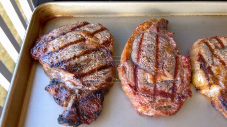 Trois succulents biftecks de côtelette présentent des marques de gril parfaites après cuisson, présentés sur une surface neutre, incarnant l'art de la cuisson.