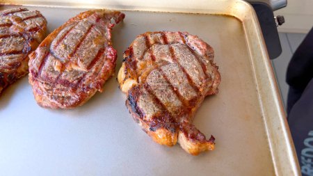 Drei saftige Ribeye-Steaks zeigen nach dem Garen perfekte Grillspuren, präsentiert auf neutraler Oberfläche und verkörpern die Kunst des Grills.