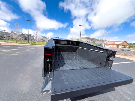 Photo for Denver, Colorado, USA-March 28, 2024-The distinctive rear end of a Tesla Cybertruck, captured in an empty parking lot, stands out against a backdrop of suburban homes under a blue sky with fluffy - Royalty Free Image
